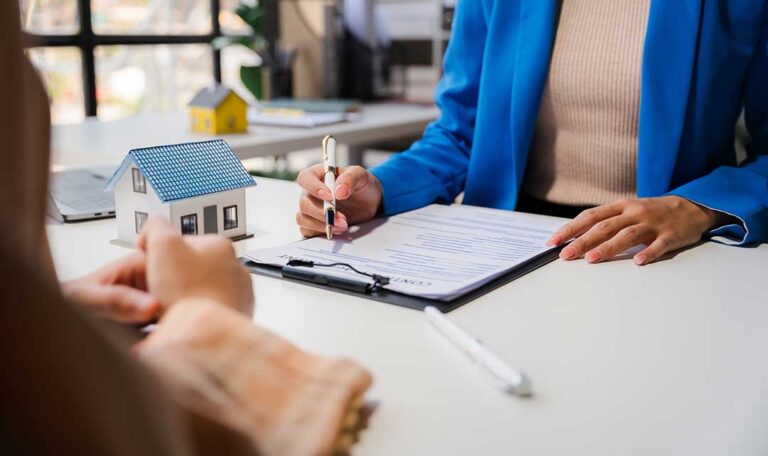 Homeowner photographs water damage while organizing receipts and repair documents at a kitchen table.